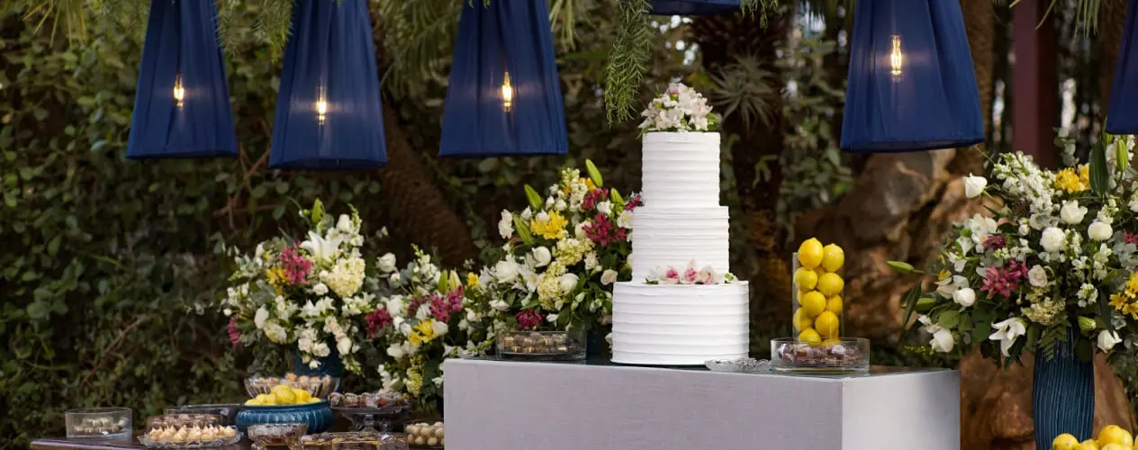 Mesa decorada com flores diversas, bolo e iluminação